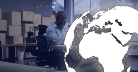 Leaning woman in blouse pointing at computer in office, with boxes, globe overlay, copy space. Collaboration, teamwork, business, modern, corporate, global, communicationの写真素材