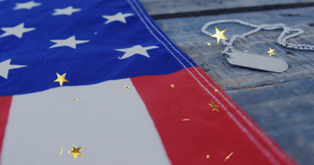Showing American flag draping over wooden tabletop with dog tags and gold star confetti, copy space. Patriotism, tribute, memorial, solemn, vintage, heritage, celebrationの写真素材