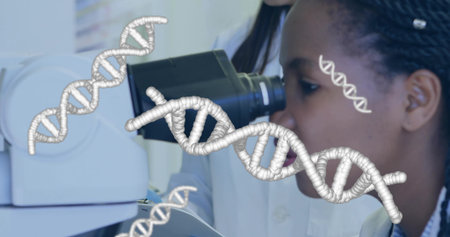 Examining female scientist in white lab coat peering into microscope in lab, with DNA graphics....