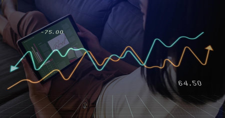 Asian woman leaning on sofa in lounge analyzing charts on tablet displaying -75.00 and line graphs....
