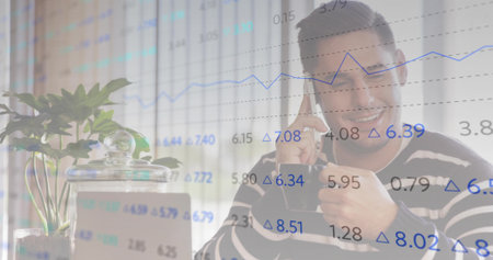 Gesturing thumbs-up Chinese man holding smartphone at office desk with data overlay, copy space....