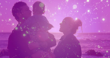 Father holding baby boy and mother watching waves at rocky shoreline, with glowing pink overlay. Family, parenthood, coastal, silhouette, tranquility, connection, serenityの写真素材