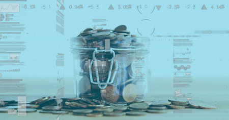 Transparent glass jar holding assorted coins on wooden surface in studio, with blue graphs. Finance, savings, investment, growth, analytics, financial data, businessの写真素材