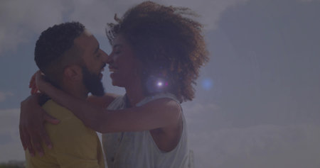 Kissing Black woman and diverse man in tank top and yellow shirt embracing outdoors, lens flare....