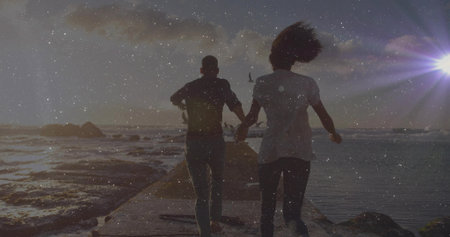 Running couple holding hands along concrete jetty at sunset, crashing waves on rocks and seabird....