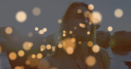 Lifting dumbbells shirtless man wearing cord necklace on rocky shoreline at dusk, with bokeh orbs. Fitness, strength, vitality, wellness, outdoor, motivational, abstractの写真素材