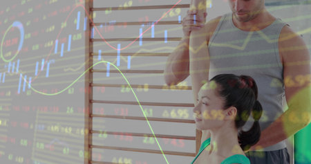 Trainer guiding stretching woman in green top on wall bars at gym, with stock chart overlay....