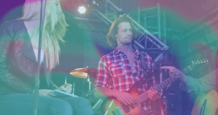 Playing electric guitar, guitarist wearing red shirt on concert stage with drums and trusses. Performance, stage, music, live, concert, lighting, musicianshipの写真素材