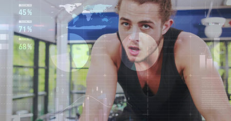 Cycling fit male leaning forward intensely at modern gym with bike and digital analytics overlays....