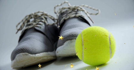 Showcasing gray athletic sneakers resting on studio surface with tennis ball and golden stars. Sport, fitness, footwear, activewear, minimalist, energetic, dynamicの写真素材
