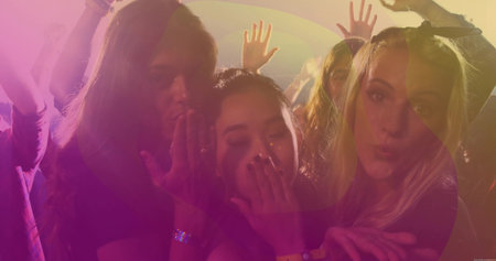 Blowing kisses three friends dancing on nightclub dance floor, with stage light haze and wristbands. Festival, celebration, nightlife, energetic, vibrant, socializing, glamourの写真素材