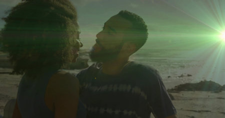 Couple facing each other wearing tie-dye t-shirt on rocky shoreline at sunset, with lens flare....