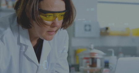 Female scientist wearing lab coat analyzing data at bench with glassware and laptop, copy space....