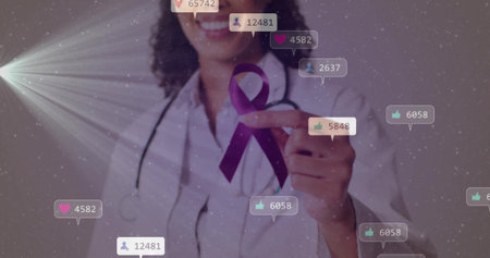 Smiling doctor wearing white coat and stethoscope pointing at purple ribbon in studio with bubbles. Healthcare, philanthropy, digital engagement, professionalism, awareness, innovation, positive attitudeの写真素材