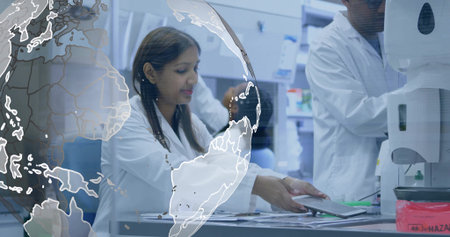 Reaching researcher grabbing digital tablet on bench at research lab, with analyzer, globe overlay. Science, innovation, collaboration, technology, precision, experimentation, developmentの写真素材