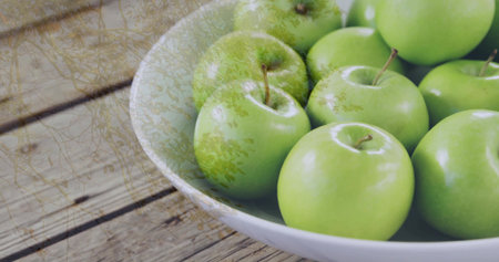 Displaying white ceramic bowl holding shiny green apples on wooden kitchen table, copy space. Fresh produce, healthy eating, rustic decor, natural light, organic, food presentation, minimalistの写真素材