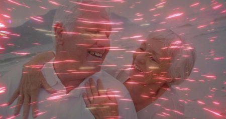 Embracing senior couple standing against light-colored wall, with dynamic pink light streaks. Romantic, connection, affectionate, contemporary, minimalism, emotional, serenityの写真素材