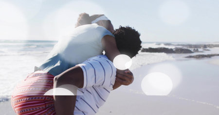 Man carrying woman piggyback along sandy beach under bright sunlight barefoot, with gentle waves. Romance, leisure, companionship, adventure, tranquility, outdoor, vibrantの写真素材