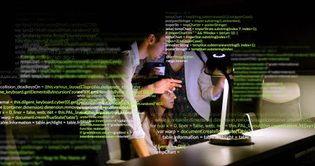 Collaborating coworkers leaning over laptop pointing at code in office at night, with lamp. Technology, innovation, teamwork, productivity, modernity, communication, startupの写真素材