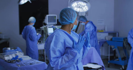 Adjusting gloves surgical nurse in blue scrubs in operating room, with monitor and surgical lights. Medical, healthcare, clinical, sterile, teamwork, precision, hospitalの写真素材