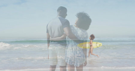 Embracing couple standing on sandy beach, with running surfer in swimsuit carrying yellow surfboard....
