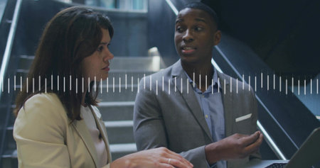 Business colleagues in suits exchanging feedback in office stairwell, with laptop, audio waveform....