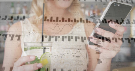 Sipping adult woman holding smartphone and analyzing overlay charts in kitchen, with smoothie jar....