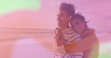 Hugging couple wearing mustard turtleneck and blue striped sweater on sandy beach, sunset glow....