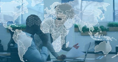 Collaborating colleagues reviewing reports and typing on laptop at desk, world map overlay, plants....