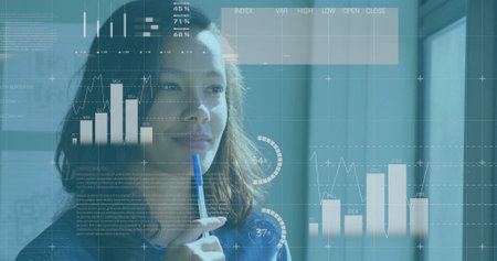 Analyzing woman wearing denim shirt holding pen to lips at office, with charts, graphs, gauges. Analytics, business, data visualization, modern, professional, urban, minimalisticの写真素材