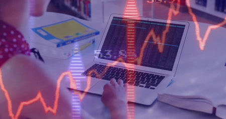 Typing teenager in red viewing charts on laptop with open book at white desk, copy space. Student, education, technology, data, learning, academic, focusの写真素材