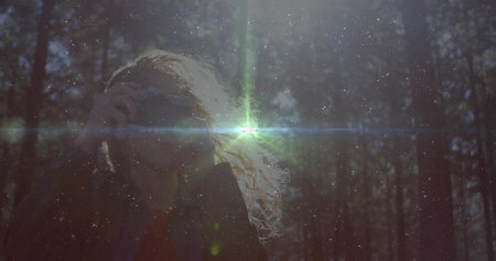 Curly haired woman taking photographs in sunlit pine forest, with lens flare and floating dust. Nature, wilderness, serenity, sunlight, exploration, artistry, outdoorの写真素材