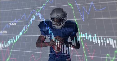 American football player in silver helmet and blue jersey holding football in studio. Athlete,...
