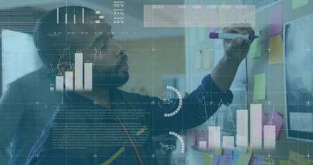 Man in blue sweater marking sticky notes with purple marker on partition in office, data analysis. Collaboration, teamwork, brainstorming, corporate, registration, innovative, productivityの写真素材