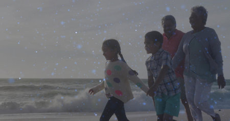 Walking grandparents and grandchildren holding hands along sandy shoreline, with gentle ocean waves....