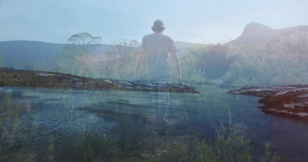Walking man wearing t-shirt, jeans and baseball cap across shallow water at lakeshore, reflections. Adventure, contemplative, tranquil, landscape, outdoors, casual, sereneの写真素材