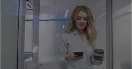 Walking woman wearing shirt holding smartphone and coffee cup in office corridor with partitions....
