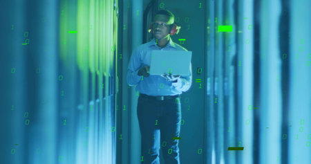 Walking African American engineer with red headphones monitoring racks in datacenter holding laptop....