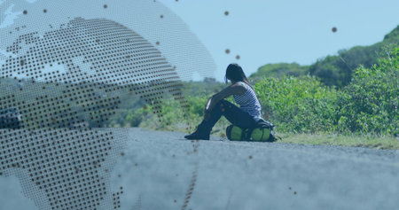 Sitting Indian woman wearing striped top on rural road edge, with green duffel bag, copy space. Solitude, adventure, exploration, landscape, travel, tranquility, natureの写真素材