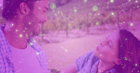 Smiling couple leaning toward each other in park orchard, with sparkly bokeh light overlay. Romantic, affectionate, outdoor, leisure, cheerful, tranquil, natureの写真素材
