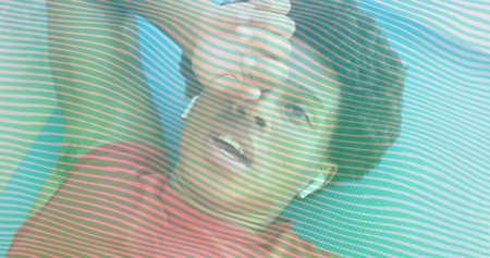 Lying fitness enthusiast wiping forehead sweat on blue mat at gym, wearing earbuds stripe overlay. Athletic, motivation, cardio, wellness, training, vibrant, enduranceの写真素材