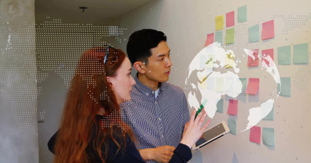 Pointing colleagues examining pastel sticky notes on office wall, with tablet and map overlay....