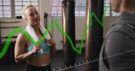 Catching breath client wearing turquoise bra and leggings in gym, with punching bags, graph overlay....
