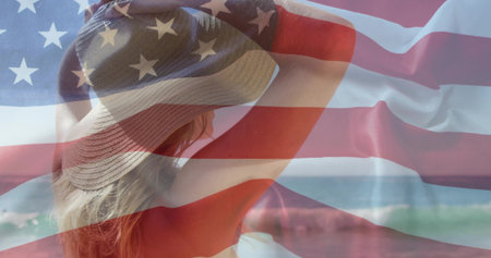Raising bikini-clad female adjusting wide-brimmed sun hat on shore with ocean waves. Beach, summer, leisure, relaxation, vibrant, scenic, fashionの写真素材