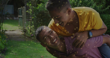 Sharing piggyback ride wearing plum polo, friend wearing yellow tee, wristwatch at garden gate. Playfulness, friendship, outdoor, leisure, vitality, casual, natureの写真素材