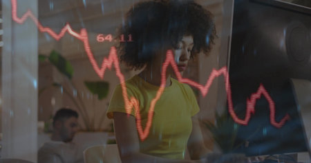 African American woman in yellow T-shirt typing on keyboard at office desk, with red graph overlay. Technology, entrepreneurship, teamwork, productivity, innovation, modernity, corporateの写真素材