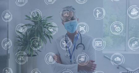 Standing doctor crossing arms wearing surgical mask and stethoscope in clinic, with digital icons. Medical, healthcare, professionalism, diagnostics, digital, wellness, technologyの写真素材