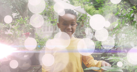 Smiling child wearing yellow shirt standing in backyard garden, with potted plants and umbrella. Children, outdoor, nature, fresh, vibrant, leisure, happinessの写真素材