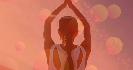 Raising Asian woman wearing white sports tank top holding mountain pose under vibrant sunset sky. Meditation, serenity, harmony, mindfulness, outdoor, silhouette, inspirationalの写真素材
