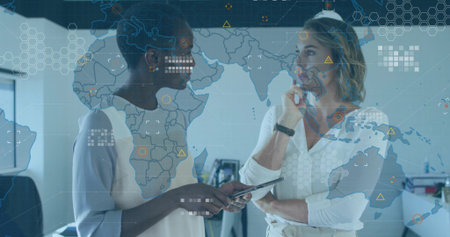 Discussing data businesswomen wearing suits using tablet at office desks, with map overlay monitors....